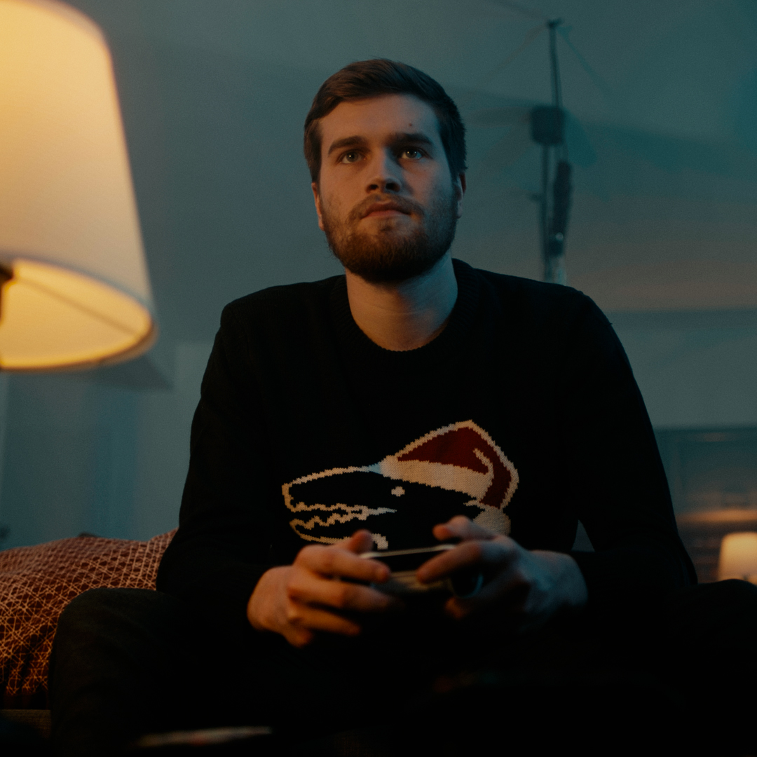 Protagonist sitzt auf Sofa und hält Controller