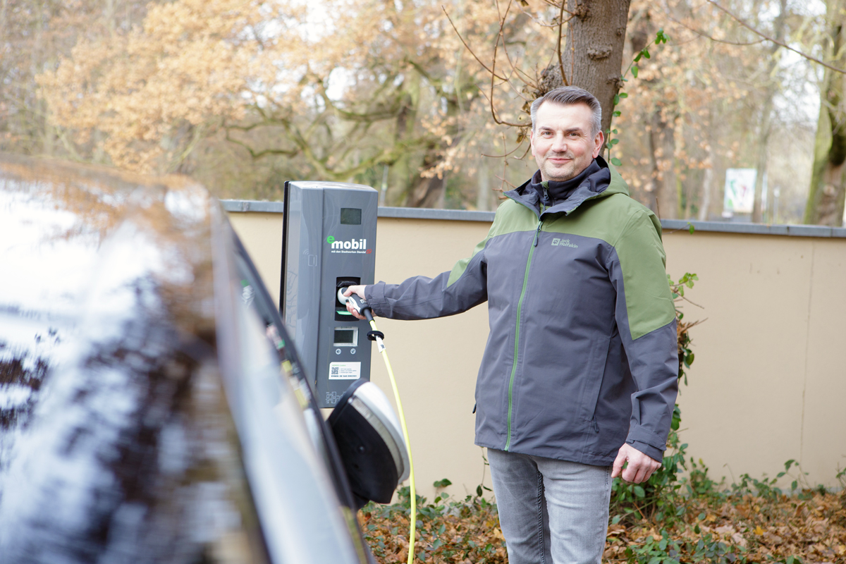 Eine Frau steht neben einem E-Auto beim Laden an einer Wall-Box - einfach, sauber, umweltbewusst - eMobil Stadtwerke Stendal GmbH für private und gewerbliche  Kunden in der Region Altmark, Sachsen-Anhalt