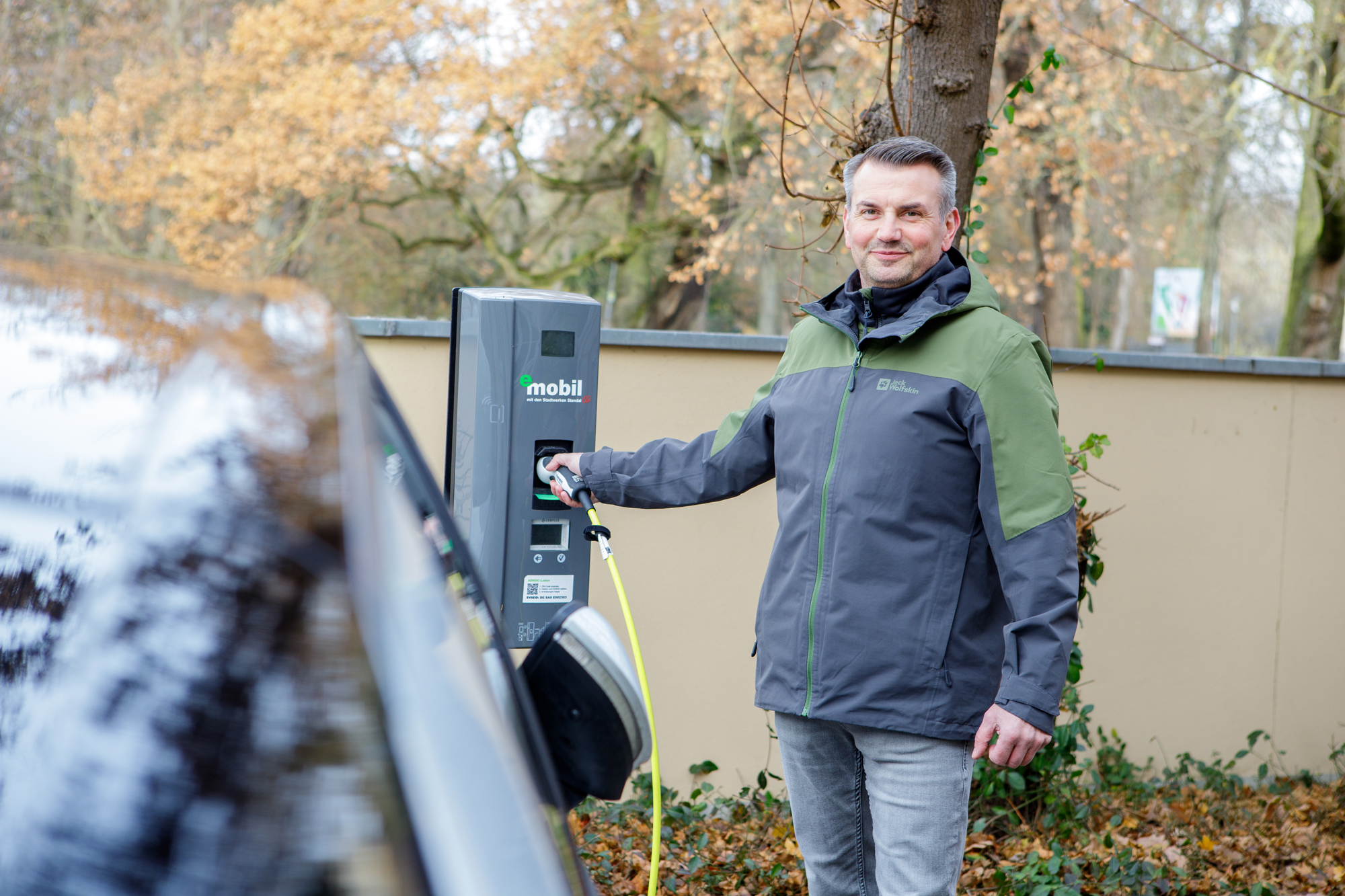 Eine Frau steht neben einem E-Auto beim Laden an einer Wall-Box - einfach, sauber, umweltbewusst - eMobil Stadtwerke Stendal GmbH für private und gewerbliche  Kunden in der Region Altmark, Sachsen-Anhalt