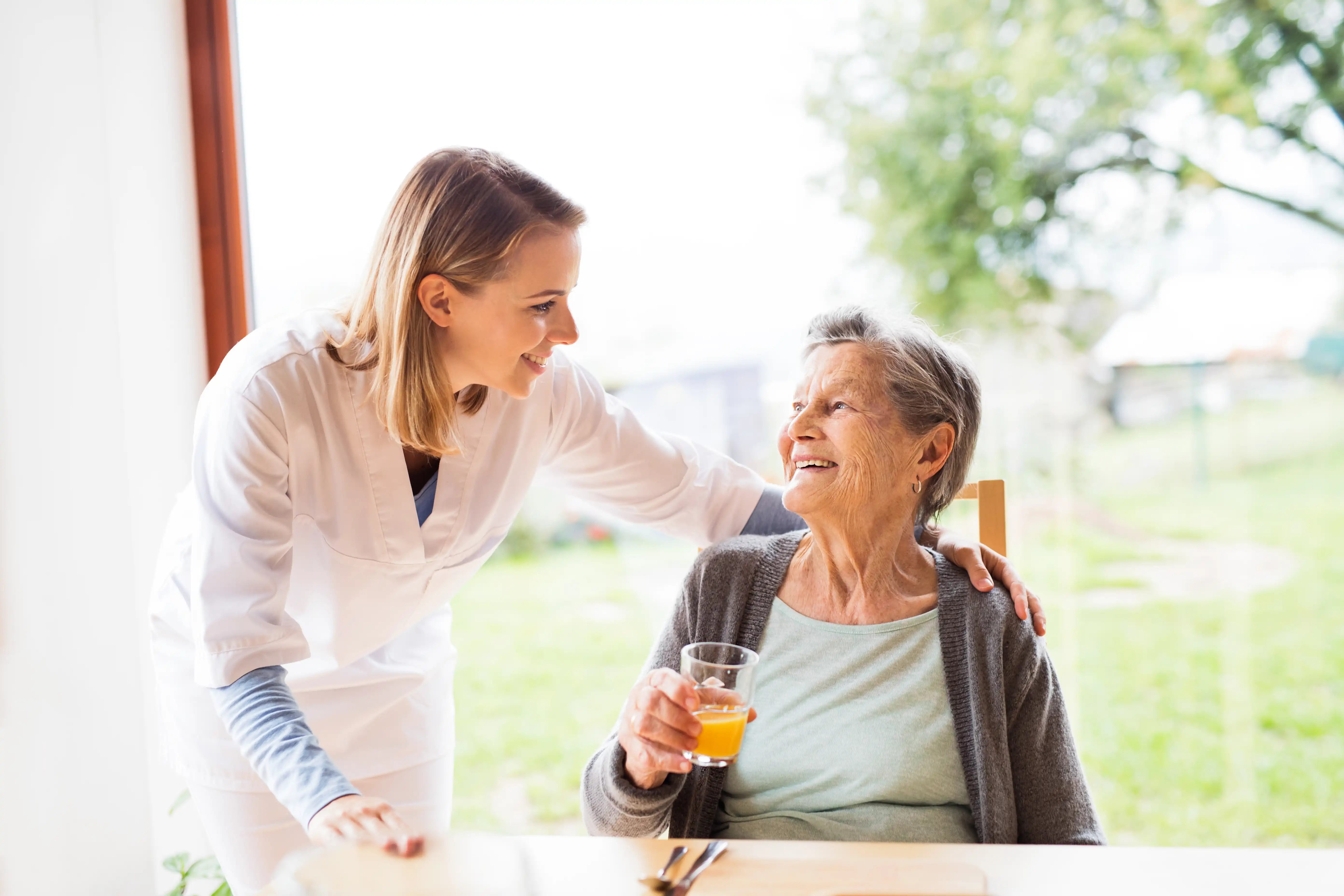 Pflegerin mit Seniorin mit Rollator im Garten