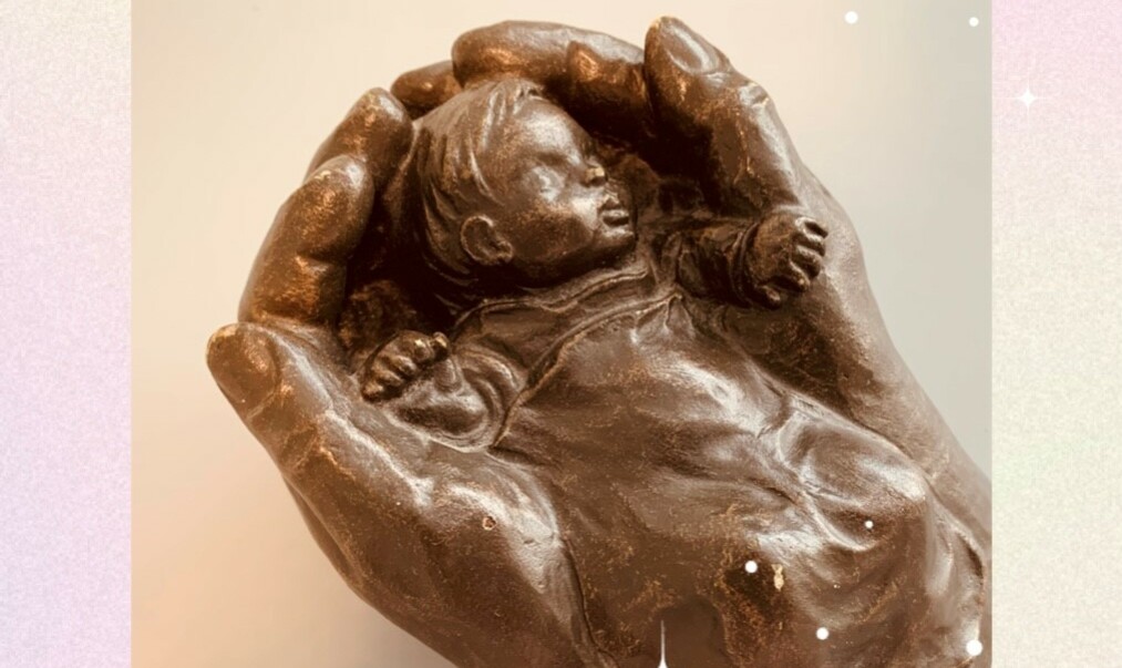 Ein Baby das in zwei Händen liegt als Figur dargestellt