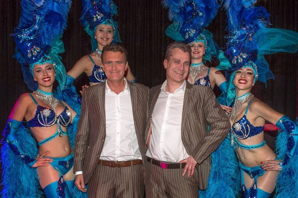 Zwei Männer posieren mit Showgirls in blauen Kostümen – Showacts buchen für Casino-Events