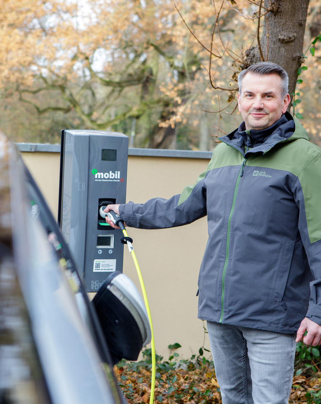 Eine Frau steht neben einem E-Auto beim Laden an einer Wall-Box - einfach, sauber, umweltbewusst - eMobil Stadtwerke Stendal GmbH für private und gewerbliche  Kunden in der Region Altmark, Sachsen-Anhalt
