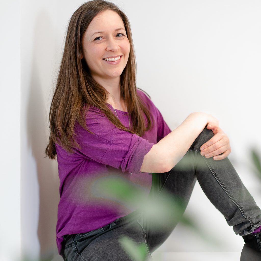 Melanie Seel, Physiotherapeutin Bahrenfeld am Bahrenpark, mit angezogenem Knie sitzend und freundlich lächelnd