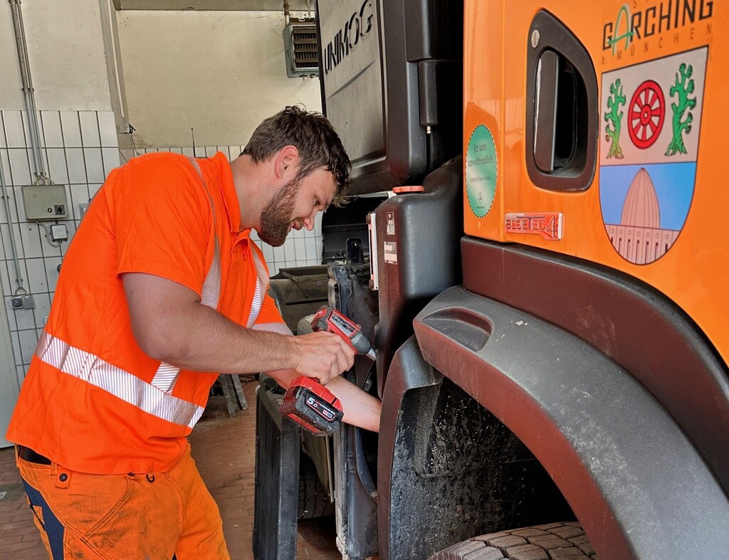 Mitarbeiter in orangefarbener Arbeitskleidung repariert ein städtisches Fahrzeug