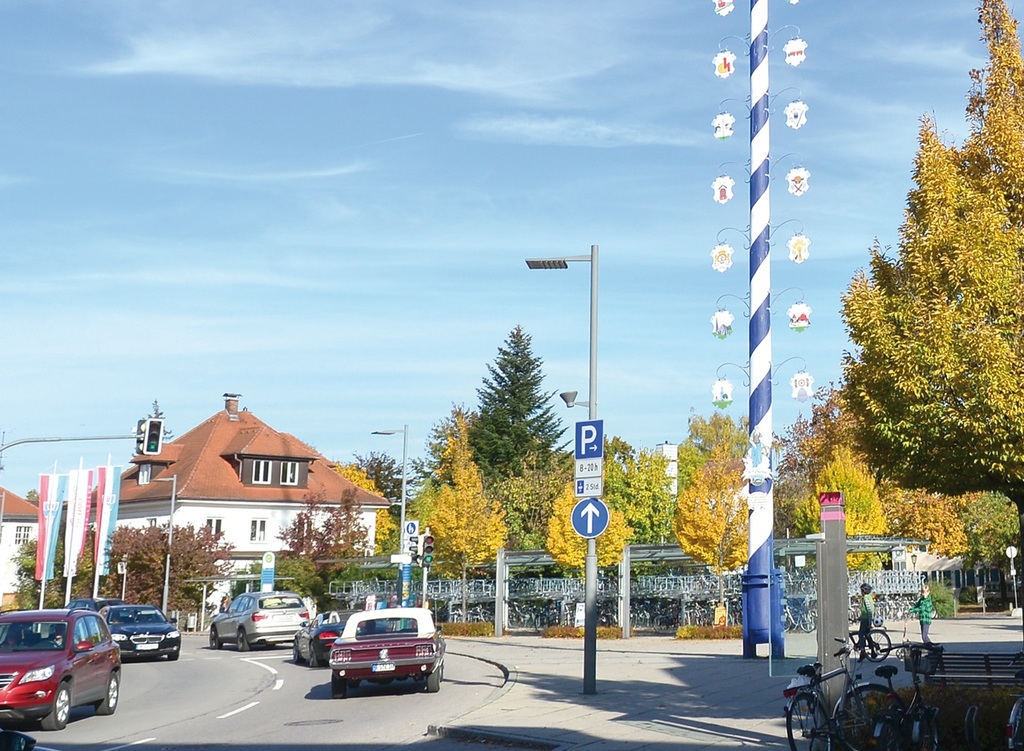 Straßenansicht mit blau-weißem Maibaum und vorbeifahrenden Autos