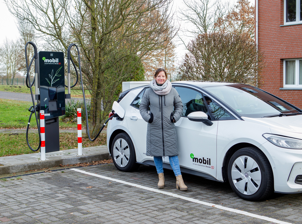 Eine Frau steht neben einem E-Auto beim Laden an einer Wall-Box - einfach, sauber, umweltbewusst - eMobil Stadtwerke Stendal GmbH für private und gewerbliche Kunden in der Region Altmark, Sachsen-Anhalt