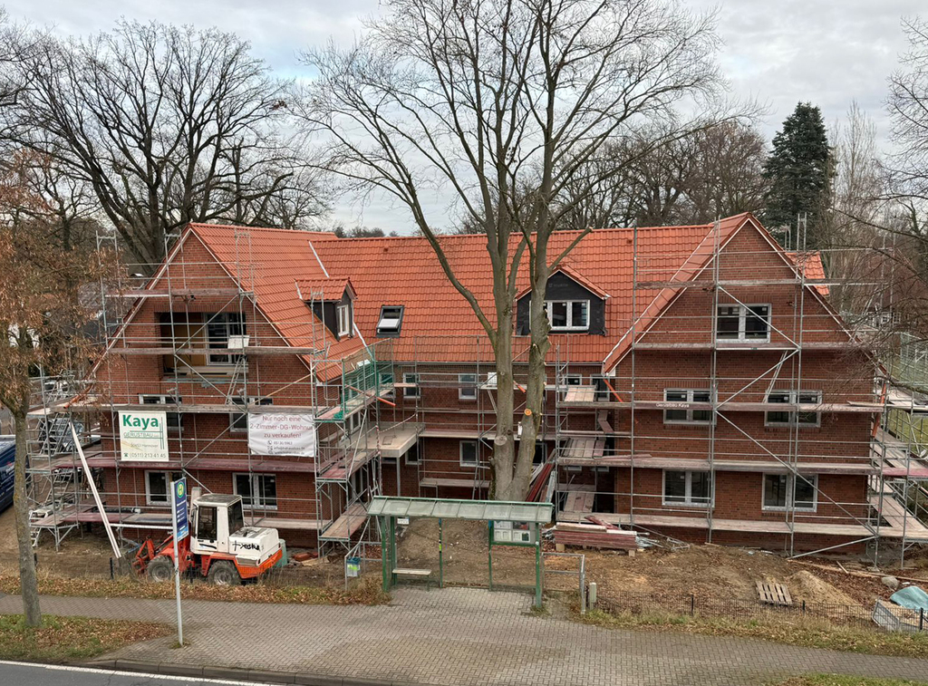 Mehrfamilienhaus im Bau mit Gerüst und Bäumen davor