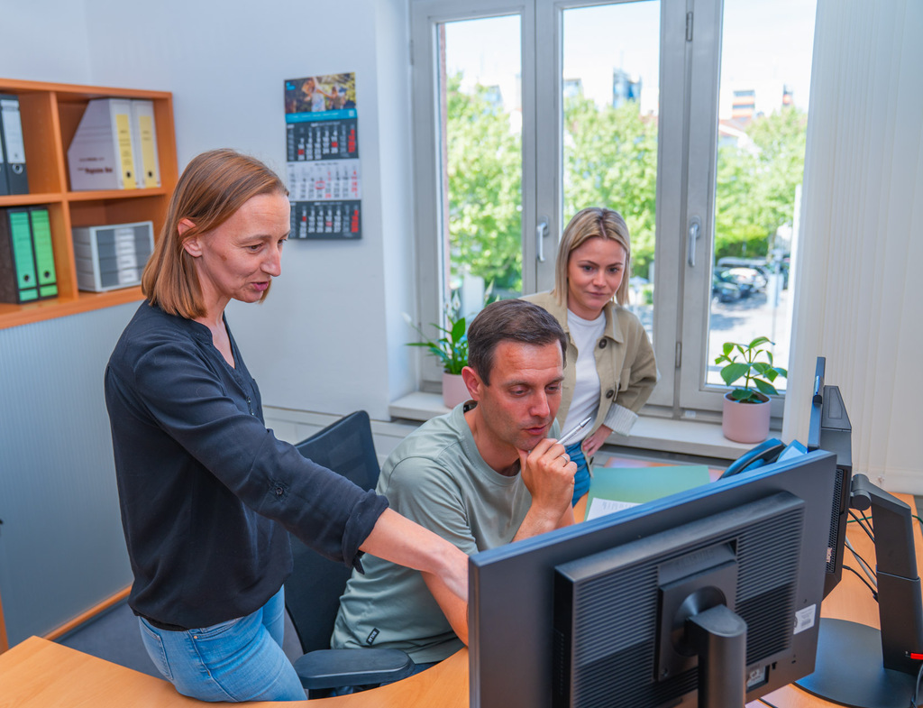 Drei Personen arbeiten gemeinsam vor einem Computerbildschirm