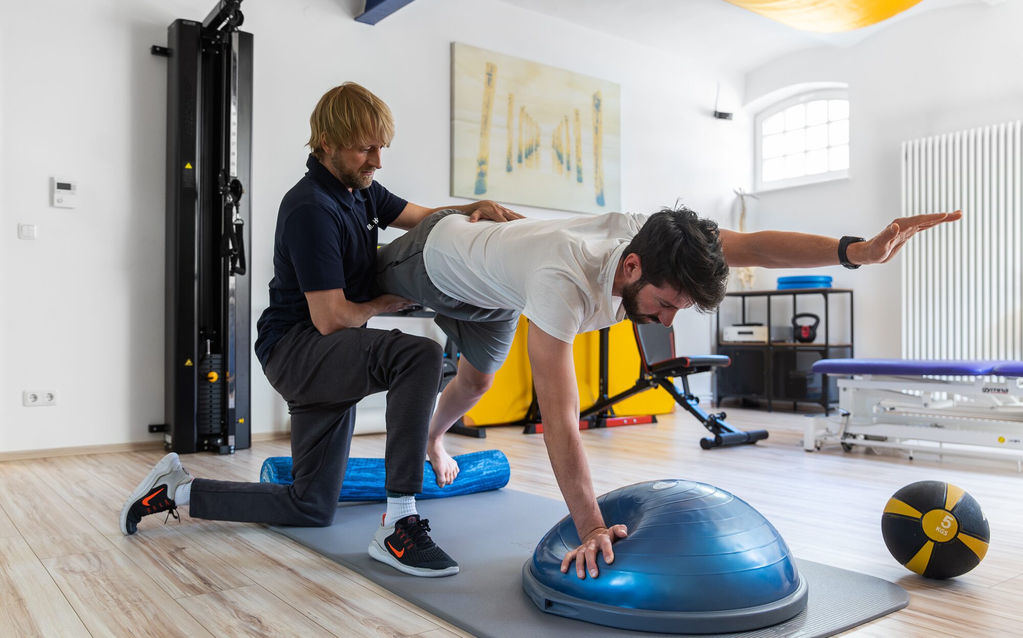  Physiotherapeut leitet Patient bei Gleichgewichtsübung mit Bosu-Ball an
