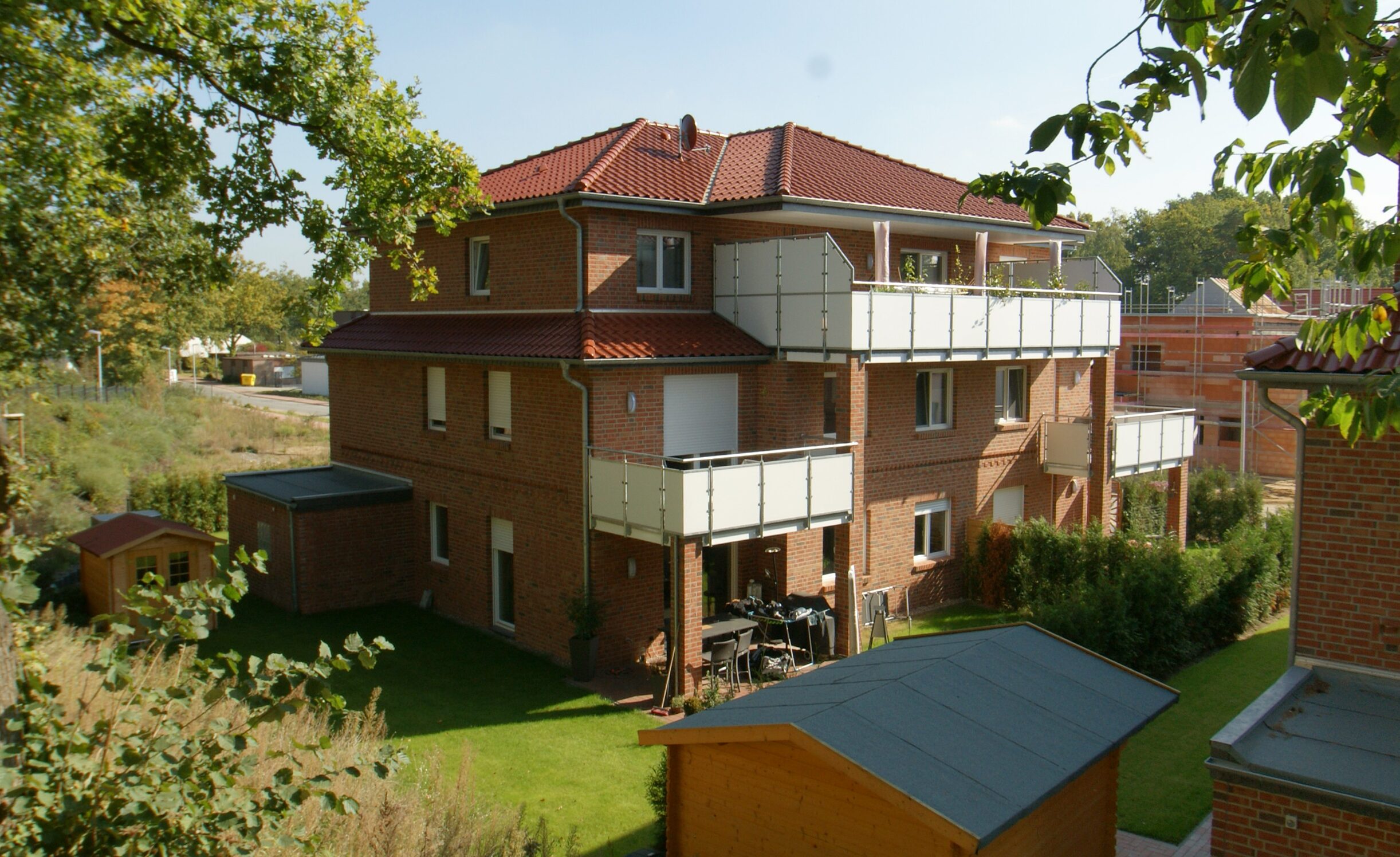 Wohnhaus mit rotem Walmdach und Balkonen in grüner Umgebung