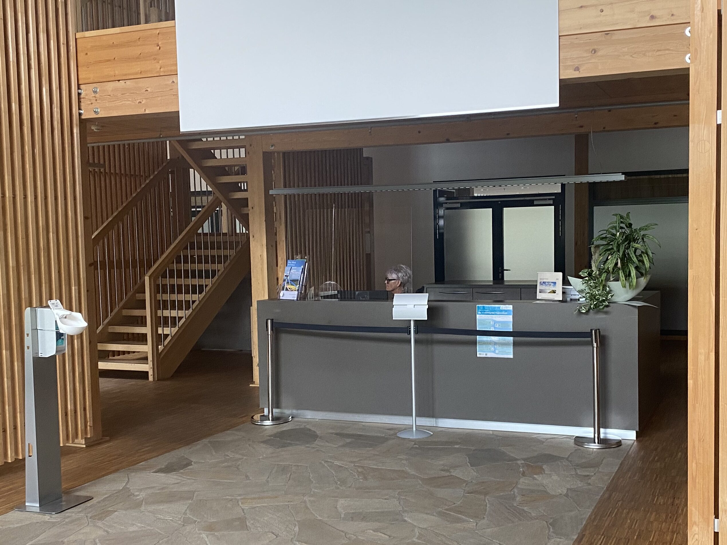 Empfang mit Holztreppe und einer sitzenden Mitarbeiterin