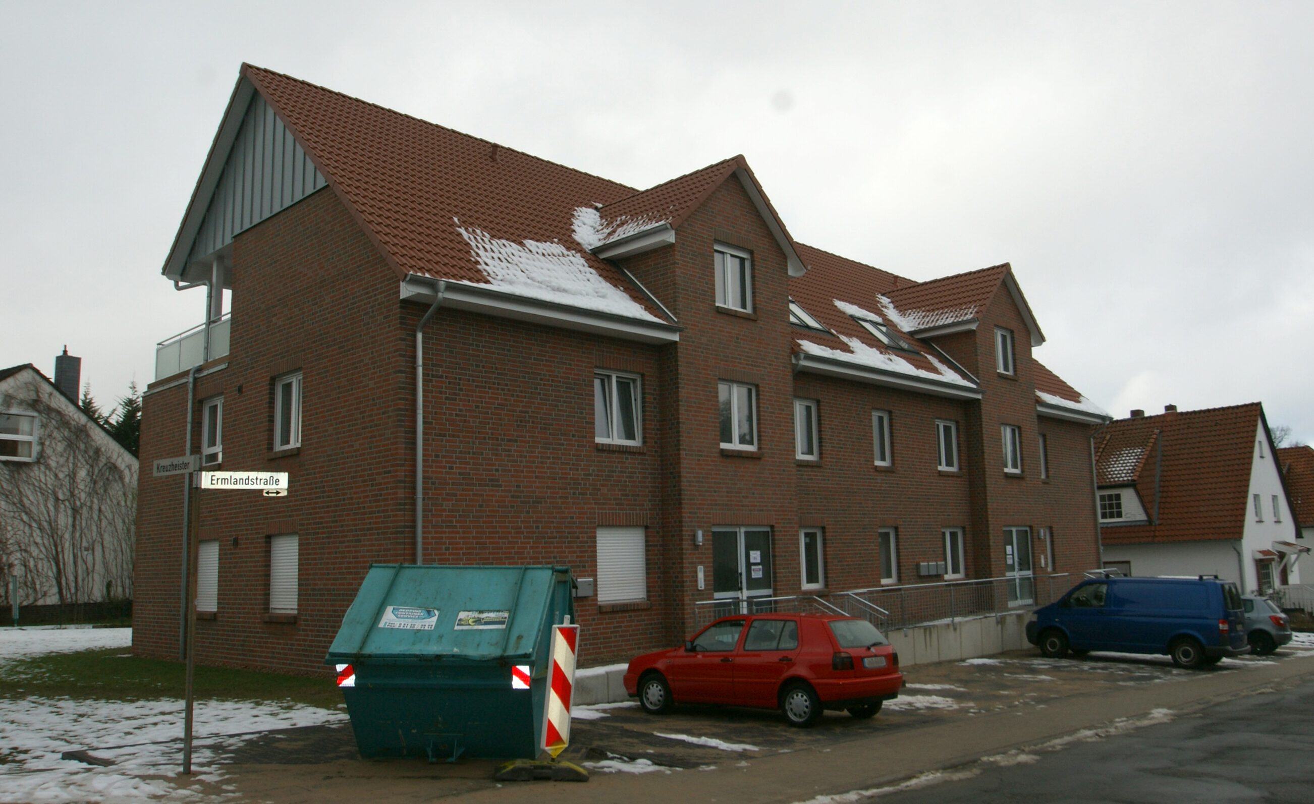 Mehrfamilienhaus mit rotem Satteldach und Schneeresten auf dem Dach