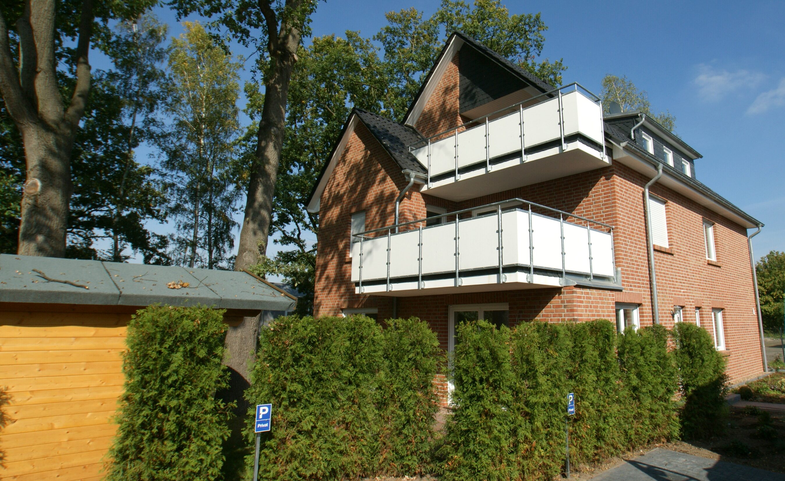 Dreigeschossiges Wohnhaus mit weißen Balkonen in grüner Umgebung