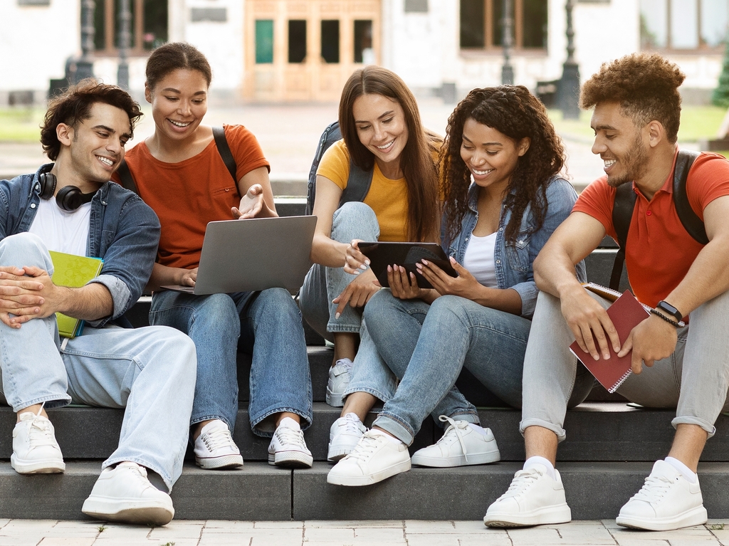 Fünf junge Menschen sitzen gemeinsam auf Treppen und arbeiten mit Laptop und Tablet