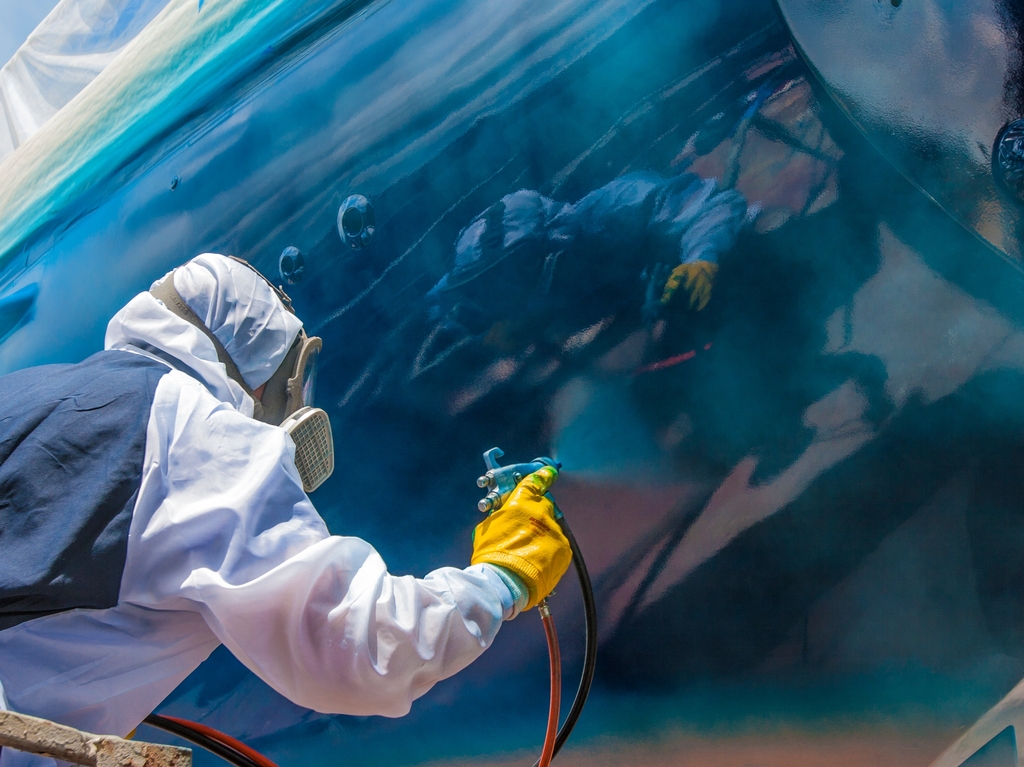 Eine Person die Schutzkleidung trägt lackiert eine Fläche blau