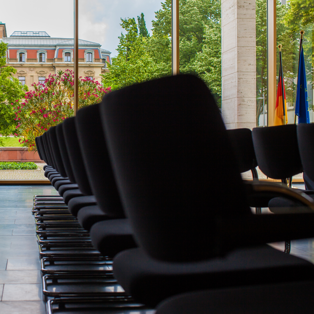 Saal mit Stuhlreihe und Blick auf Garten und Flaggen