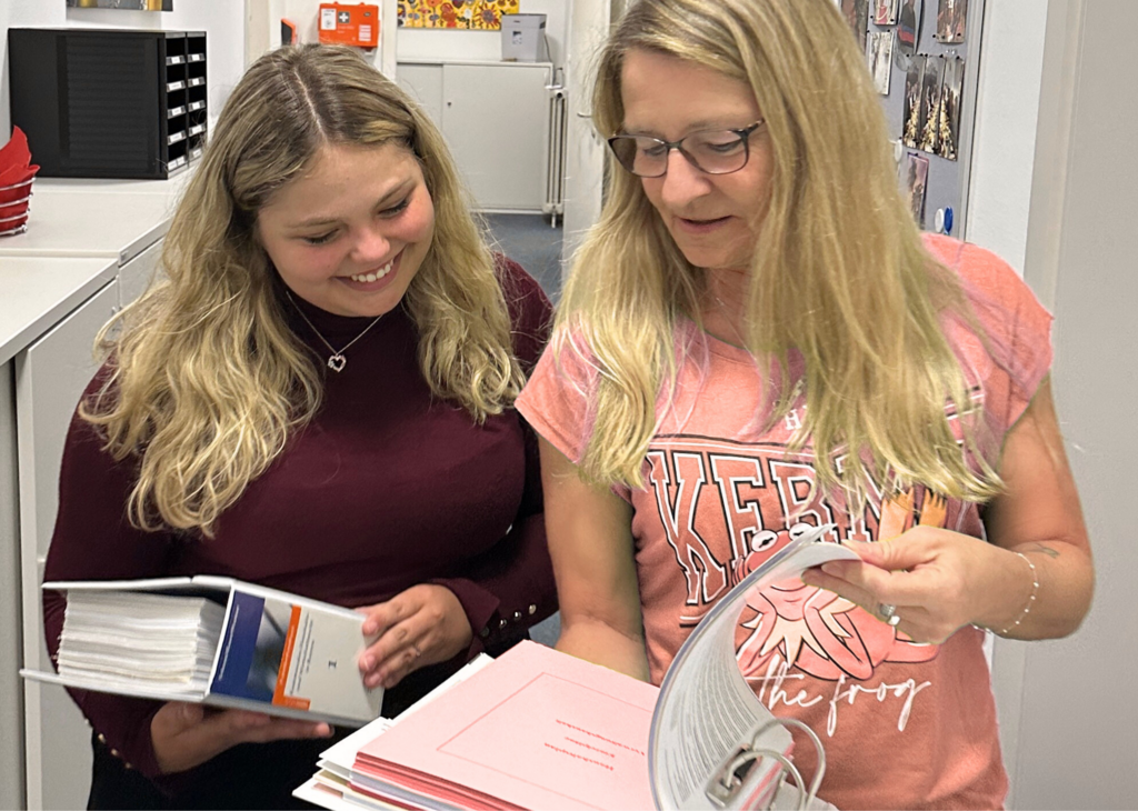 Zwei Mitarbeiterinnen sehen gemeinsam Unterlagen in dicken Aktenordnern durch