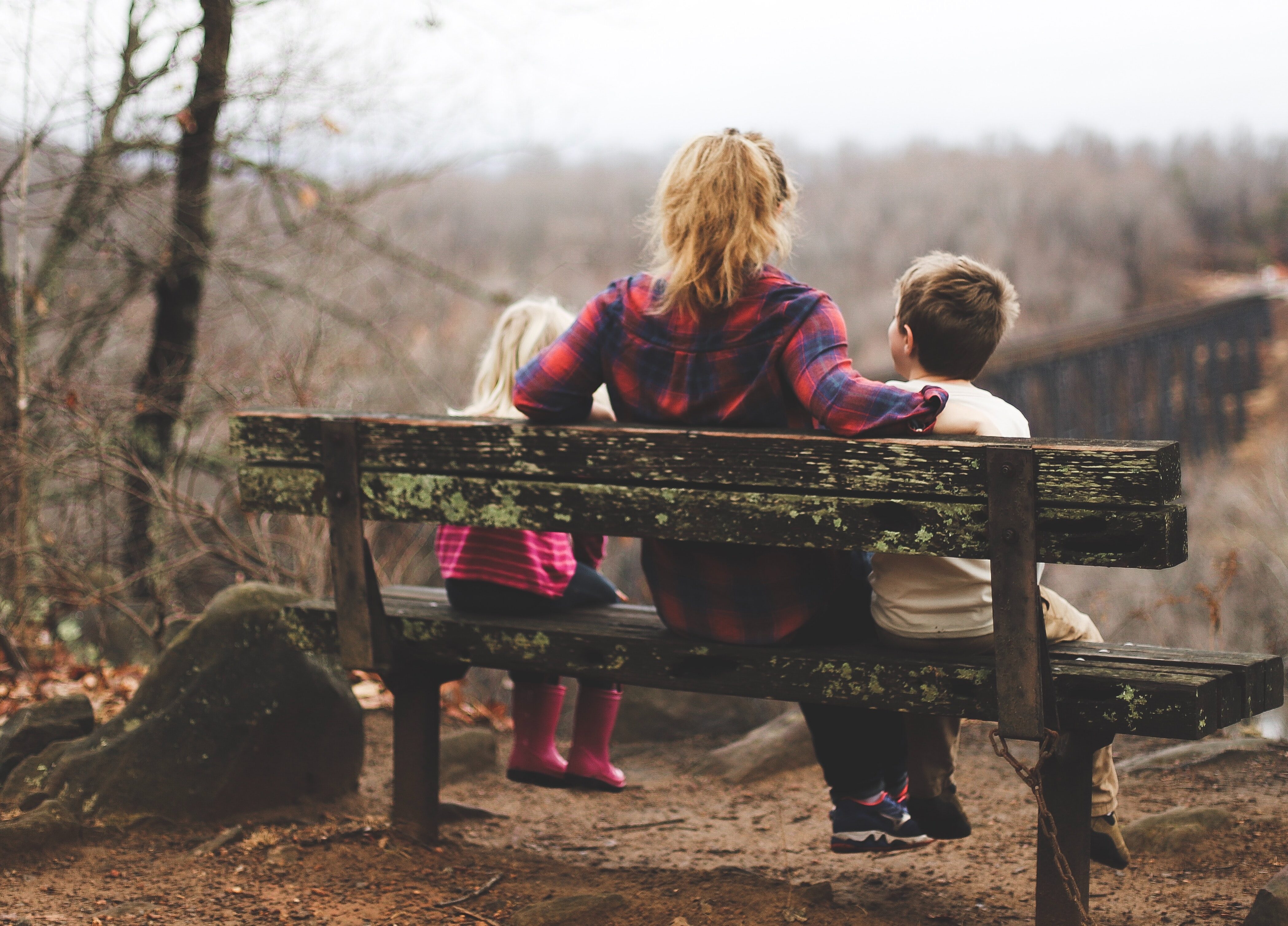 Mutter mit zwei Kindern sitzt auf einer Bank und schaut auf eine herbstliche Waldlandschaft