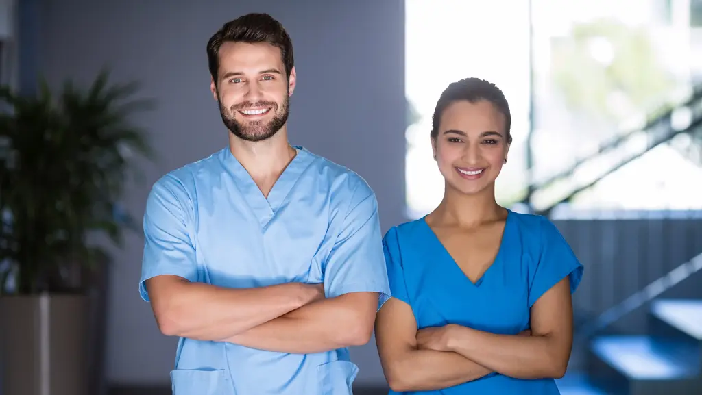 Pfleger und Pflegerin lächeln in Kamera in Arbeitskleidung