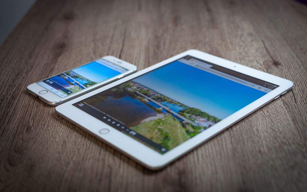 iPad und iPhone liegen mit sichtbar geöffneter Website auf einem Holztisch.