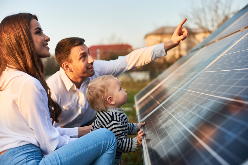 Der Mensch zeigt seiner Familie die Solarpaneele auf dem Grundstück nahe dem Haus an einem warmen Tag.