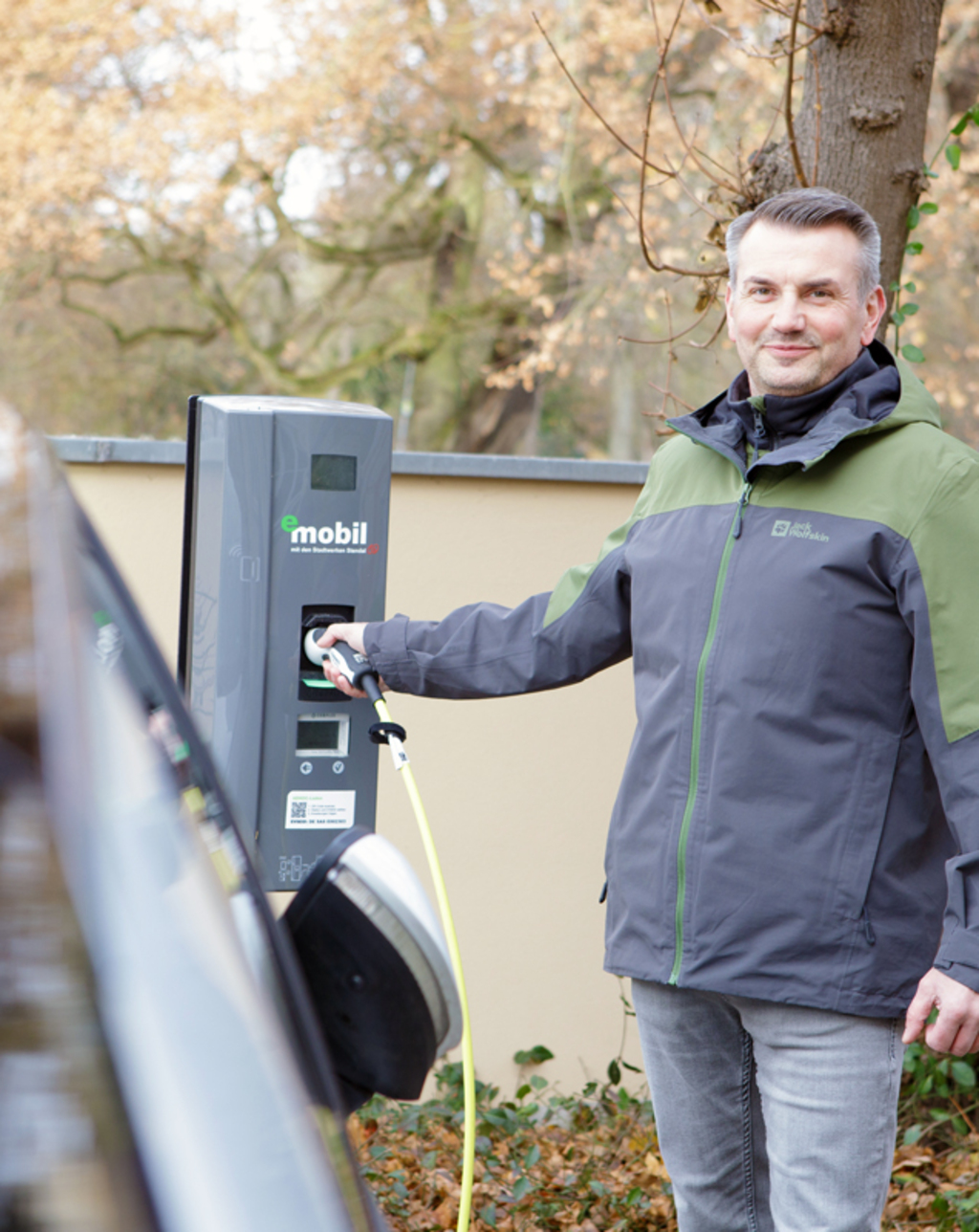 Eine Frau steht neben einem E-Auto beim Laden an einer Wall-Box - einfach, sauber, umweltbewusst - eMobil Stadtwerke Stendal GmbH für private und gewerbliche  Kunden in der Region Altmark, Sachsen-Anhalt