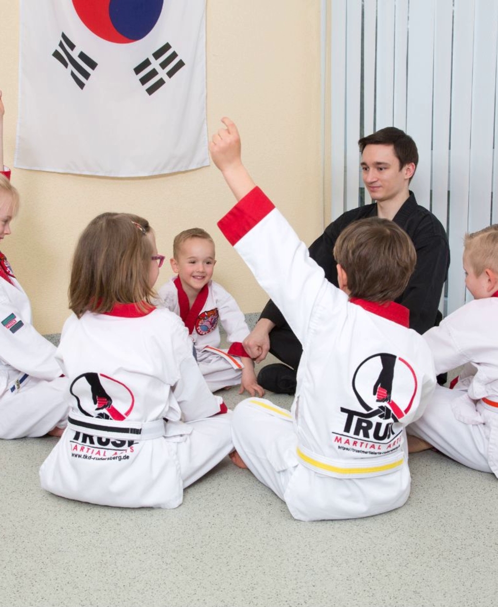 Kinder sitzen im Kreis mit ihrem Taekwando Lehrer