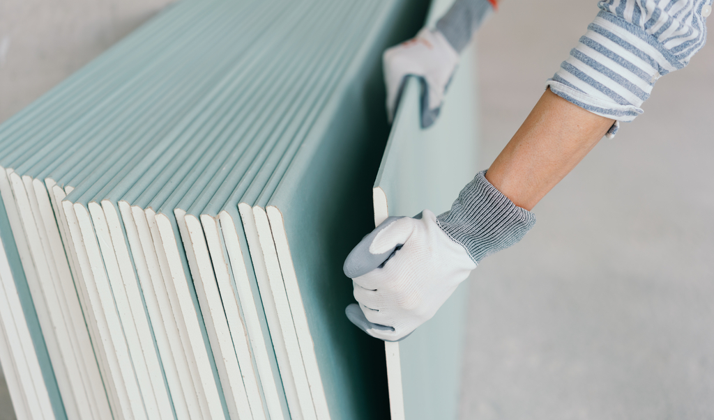Person mit Schutzhandschuhen greift in Nahaufnahme an den Händen nach einer Spanplatte für den Innenausbau