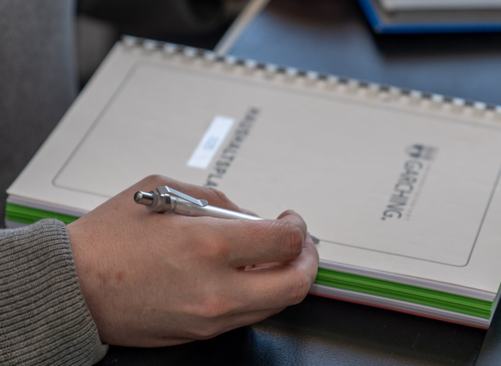 Hand mit Kugelschreiber über einer gebundenen Broschüre der Stadt Garching