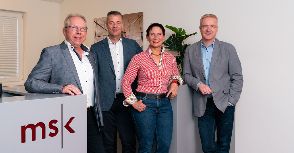 Gruppenbild der Geschäftsführung mit Ernst Meyer, Karsten Schmidt, Hendrik Meyer und Katrin Meyer vor einem hellen Hintergrund in der Kanzlei und neben einem Tresen mit msk-Logo