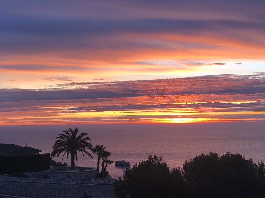 Leuchtend roter Sonnenuntergang über dem Meer mit Palmen und Klippen im Vordergrund