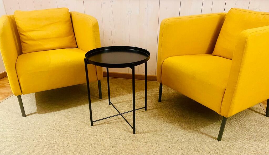 Zwei gelbe Sessel mit schwarzem Beistelltisch auf einem Teppich