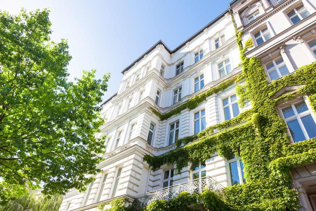 Mehrstöckiges Wohnhaus mit grüner Fassadenbepflanzung und blauem Himmel im Hintergrund.