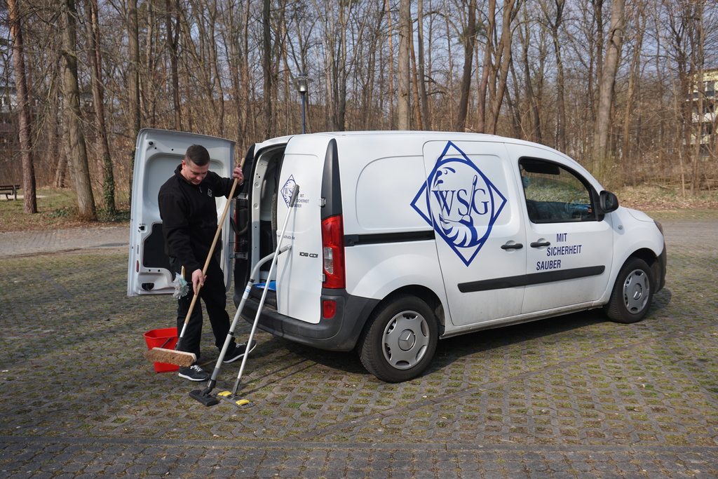 WSG-Mitarbeiter lädt Reinigungsgeräte aus einem weiß beklebten Firmenfahrzeug im Außenbereich.