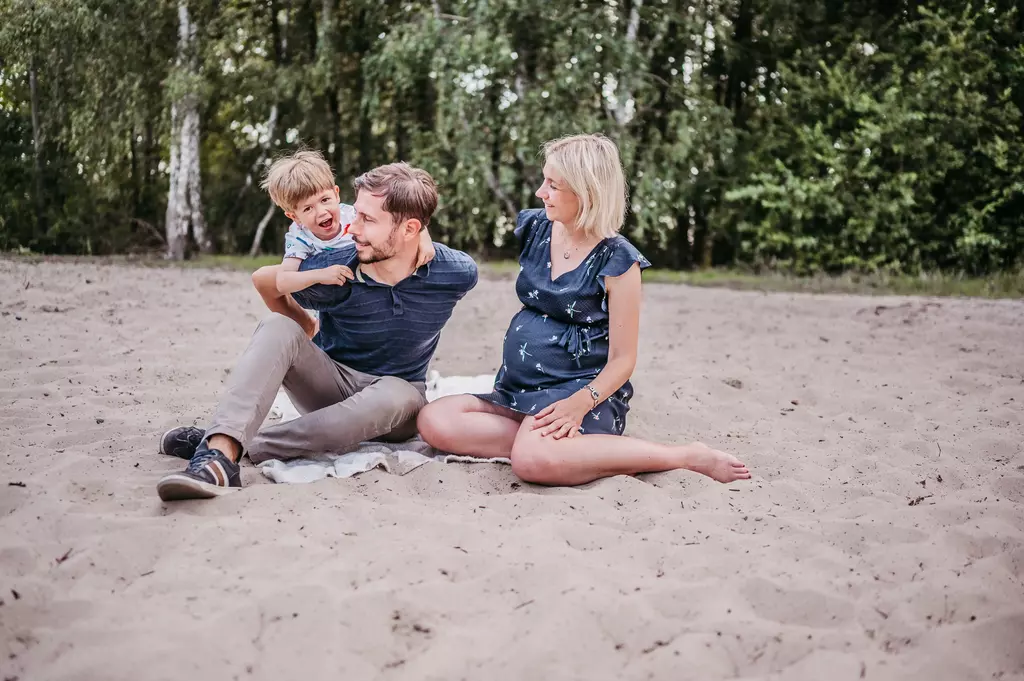 Eine Familie mit Kind während einer Familienfotografie in Berlin. Der Fotograf lässt die Familie zusammen im Sand sitzen und toben. 