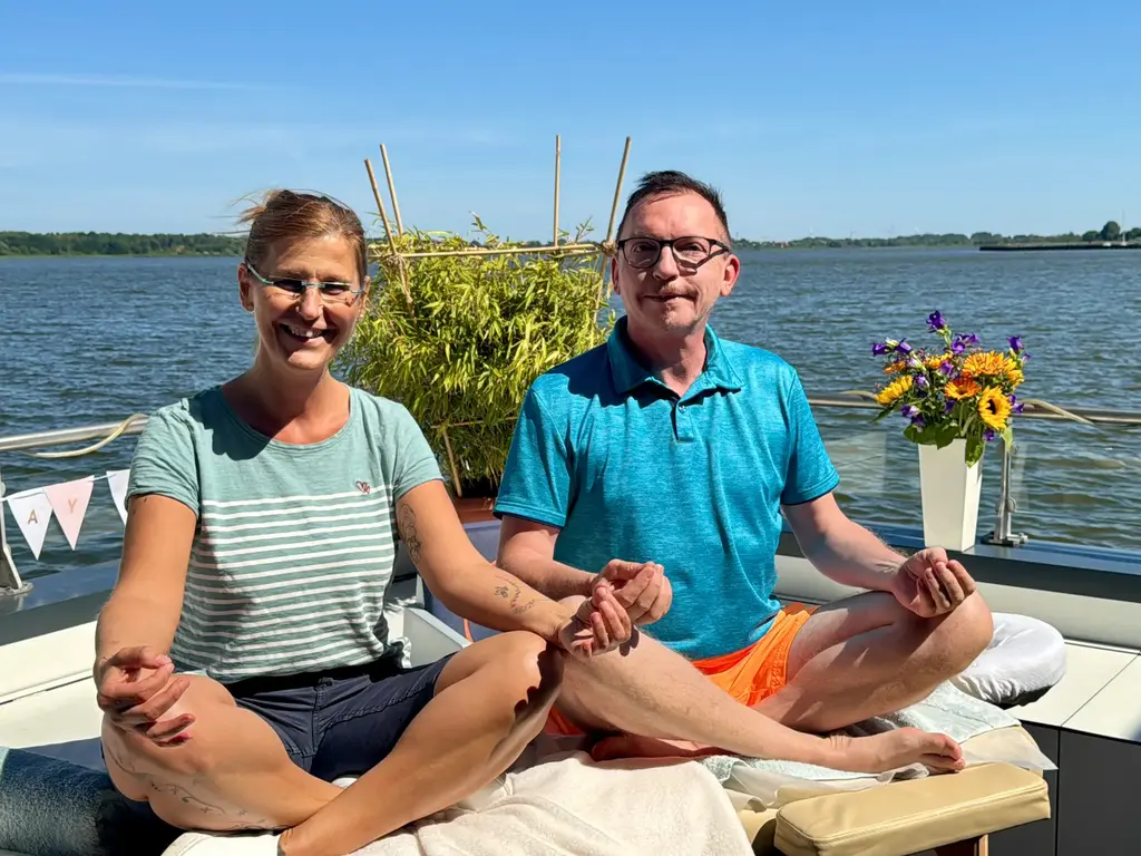 Zwei Menschen meditieren auf dem Hausboot.