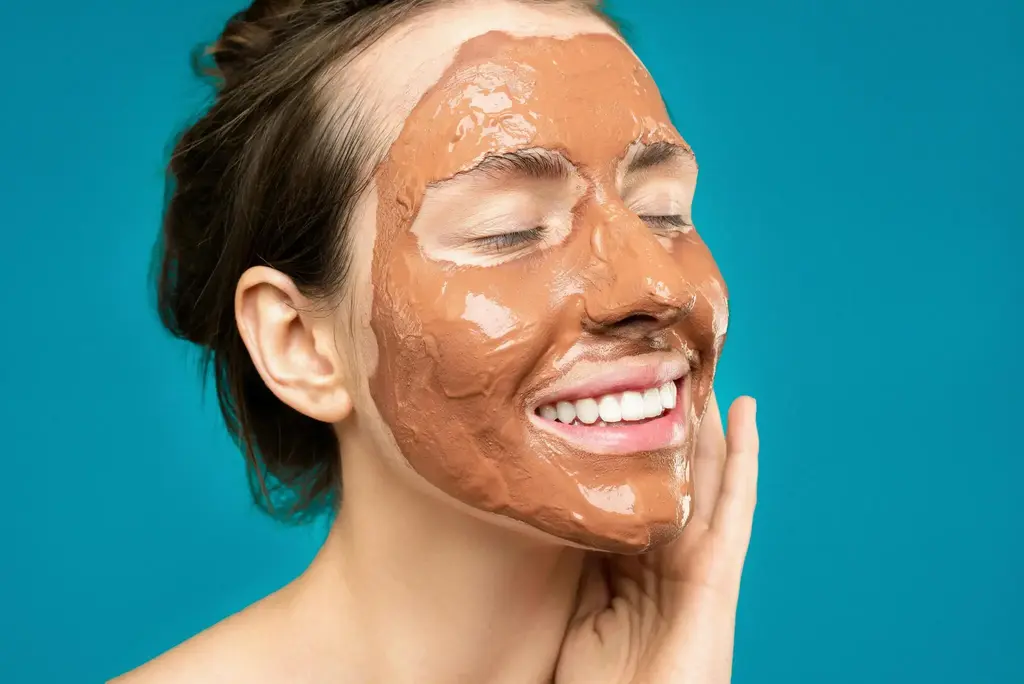 Smiling woman with clay facial mask for skincare  