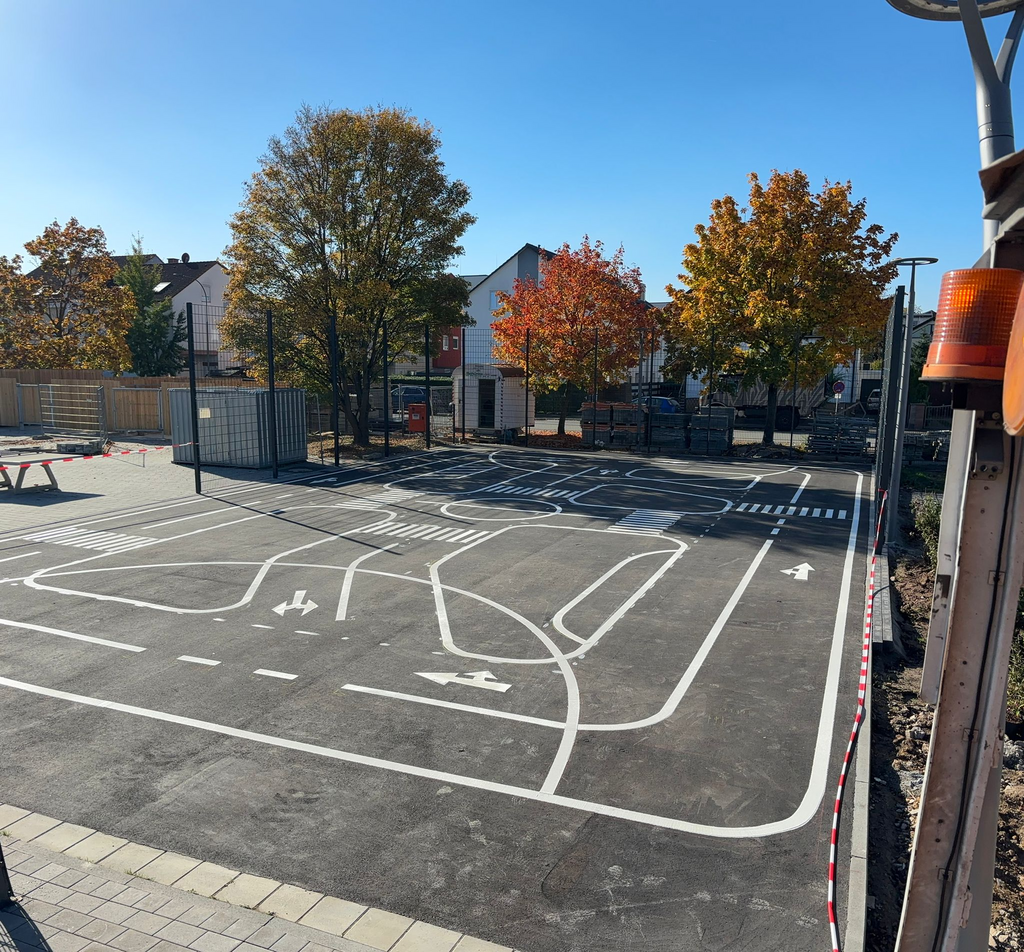 Asphaltierte Übungsfläche mit weißen Fahrbahnmarkierungen, Kreuzungen und Fahrspuren, genutzt für Verkehrserziehung und Fahrübungen.