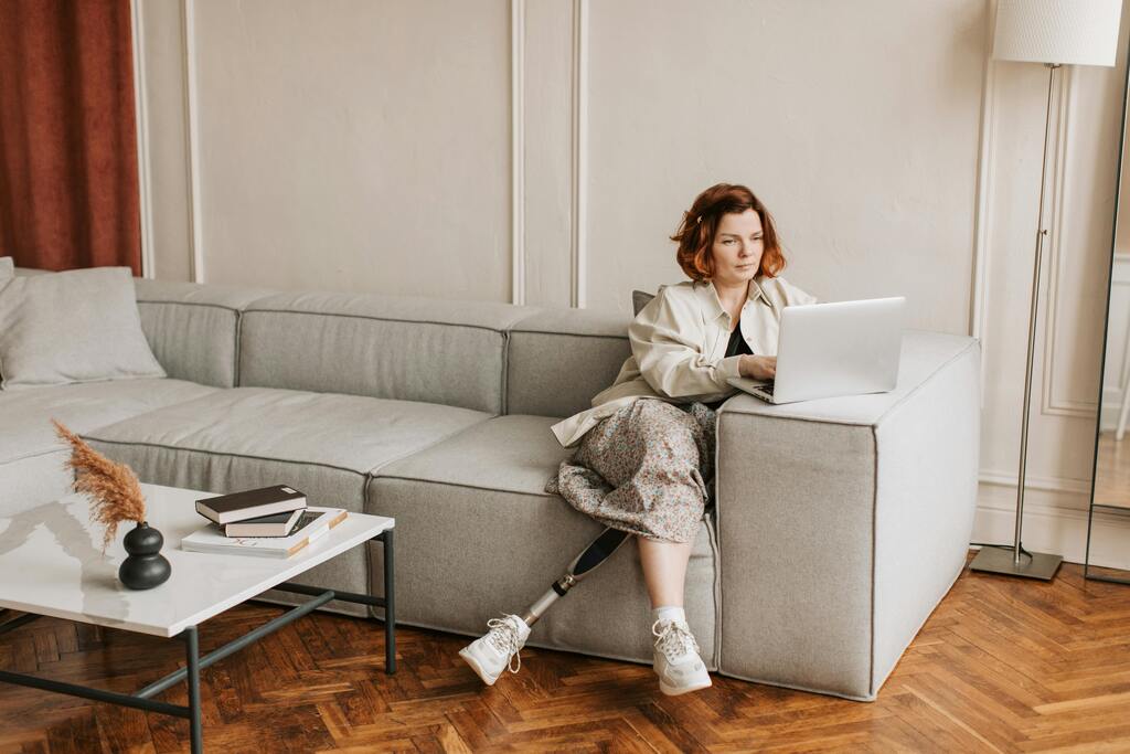Frau mit Beinprothese sitzt auf der Couch am Laptop