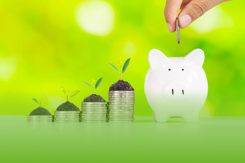 Kostenersparnis Elektroauto - wachsende Münzstapel mit grünen Pflanzen und Sparschwein vor grünem Hintergrund