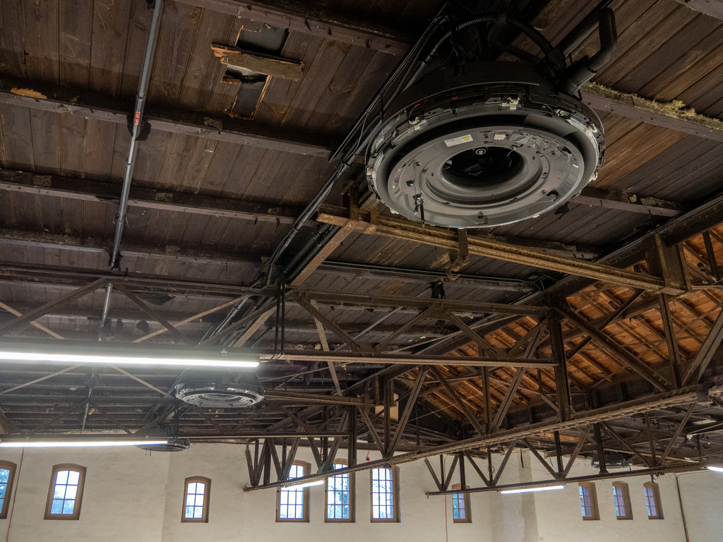 Unverkleidete Wärmepumpen-Decken-Kassette, schwarz lackiert, an der Decke einer historischen Fabrikhalle