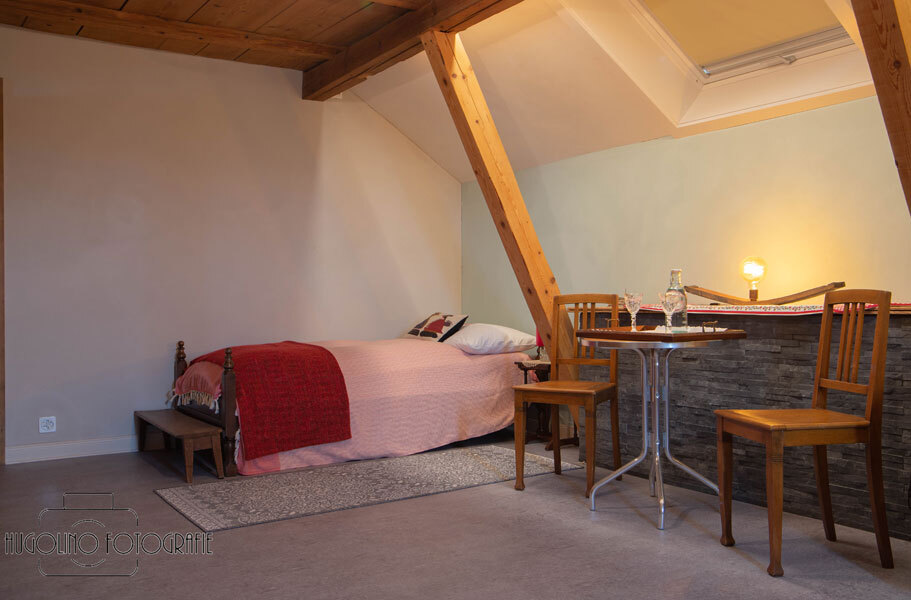 Zimmer mit Bett an der hinteren Wand und 2 Holzstühlen mit Tischchen