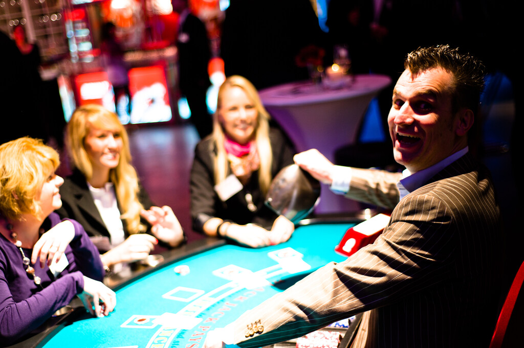 Feiernde Gäste in Abendgarderobe an Casino-Tischen bei einem stimmungsvollen Event mit festlicher Lichtdekoration von Rent-A-Casino