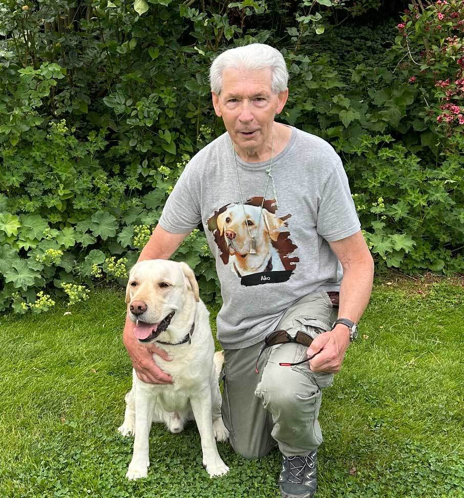 Ein älterer Mann kniet neben seinem Labrador