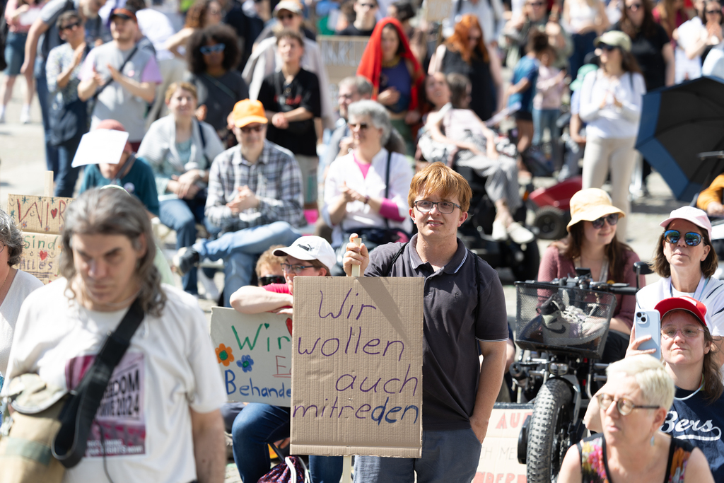 Protestplakat mit der Aufschrift „Disability Rights Are Human Rights“, gehalten von einer Menschenmenge bei einer Demonstration.