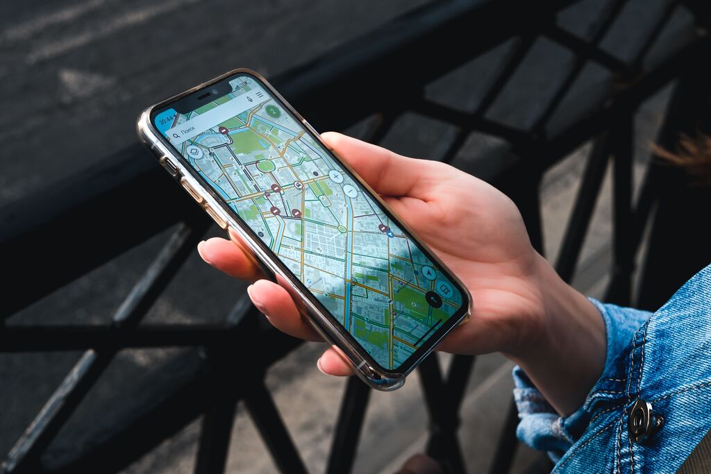 Eine Frau befindet sich an einem Geländer an der Straße und hält ein Smartphone mit geöffneter Google Maps App in der Hand.
