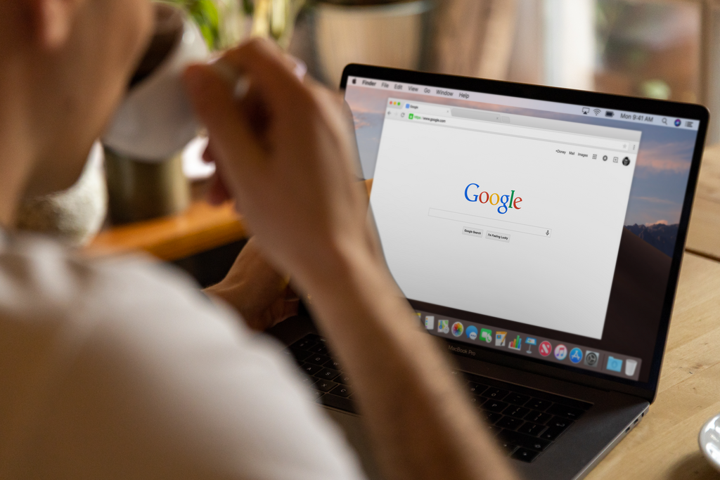 Ein Mann sitzt, Kaffee trinkend, vor einem silbernen Laptop mit geöffneter Google-Suche-Website.