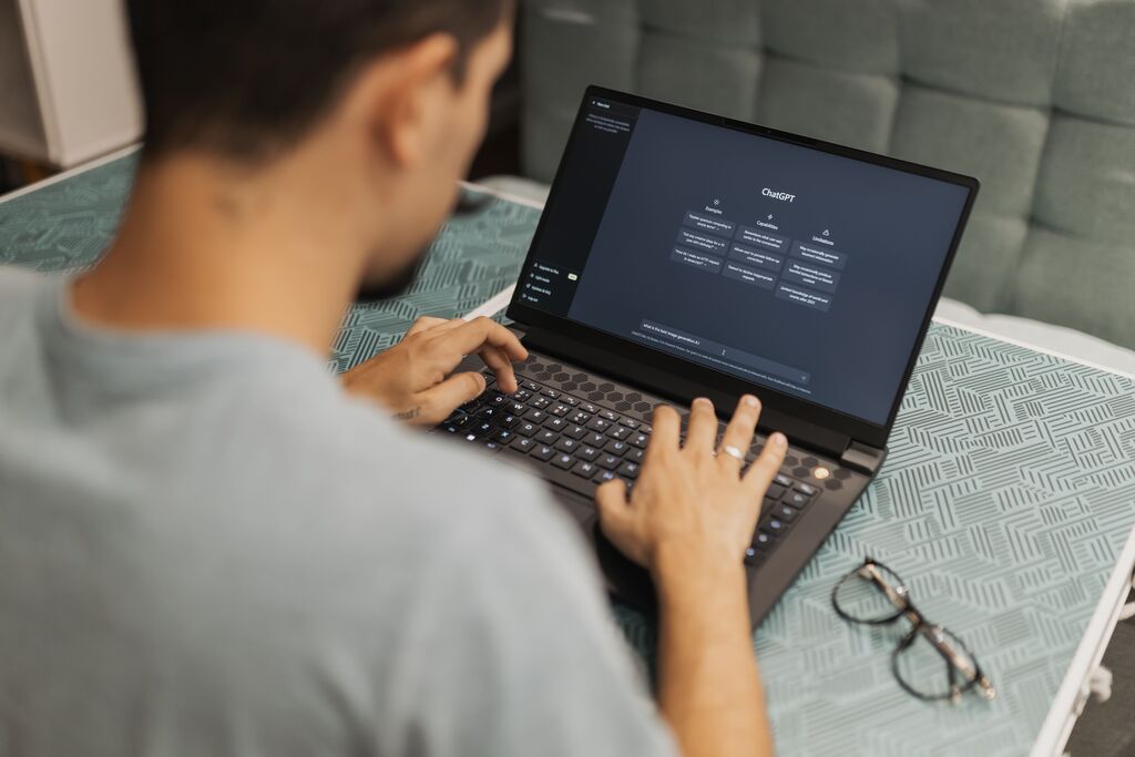 Mann, der einen Laptop mit KI-Schnittstelle benutzt und konzentriert tippt, in einem Innenraum, mit einer Brille neben sich