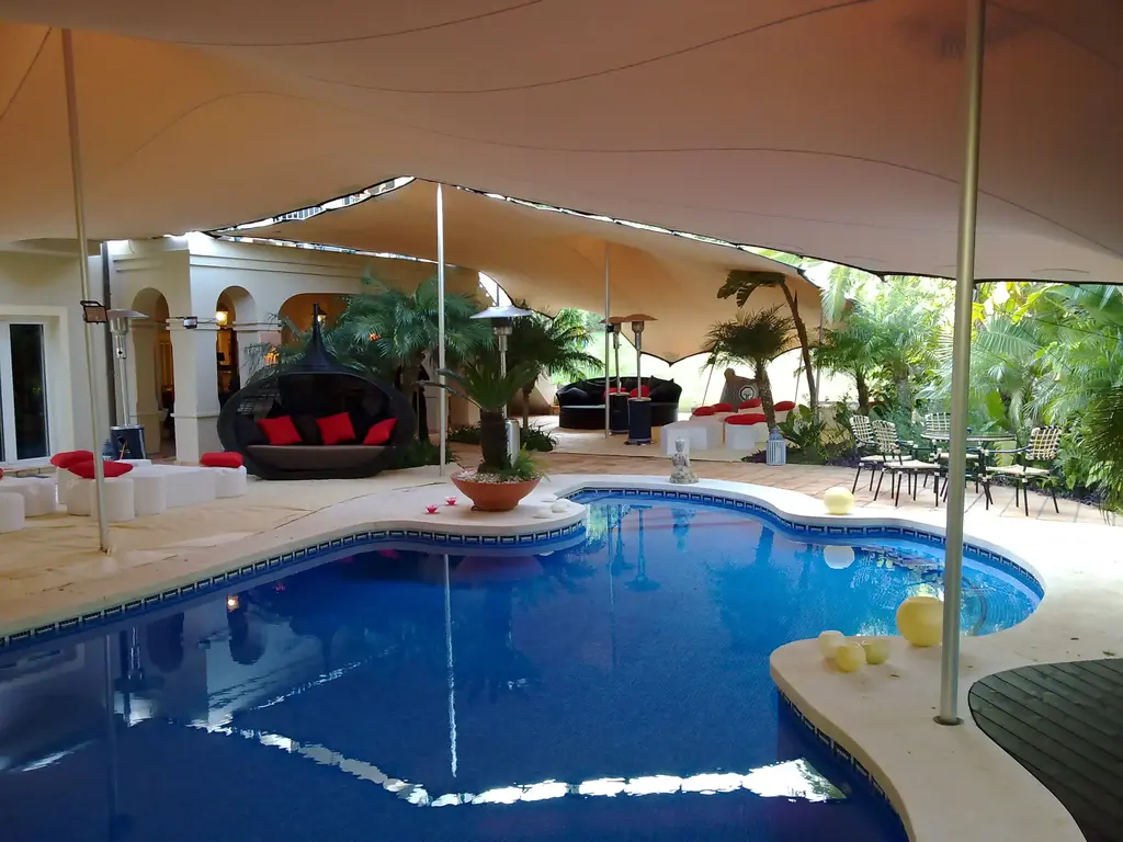 Ein Zelt steht über einem Pool, umgeben von Liegen und Pflanzen, ideal für Veranstaltungen im Freien.